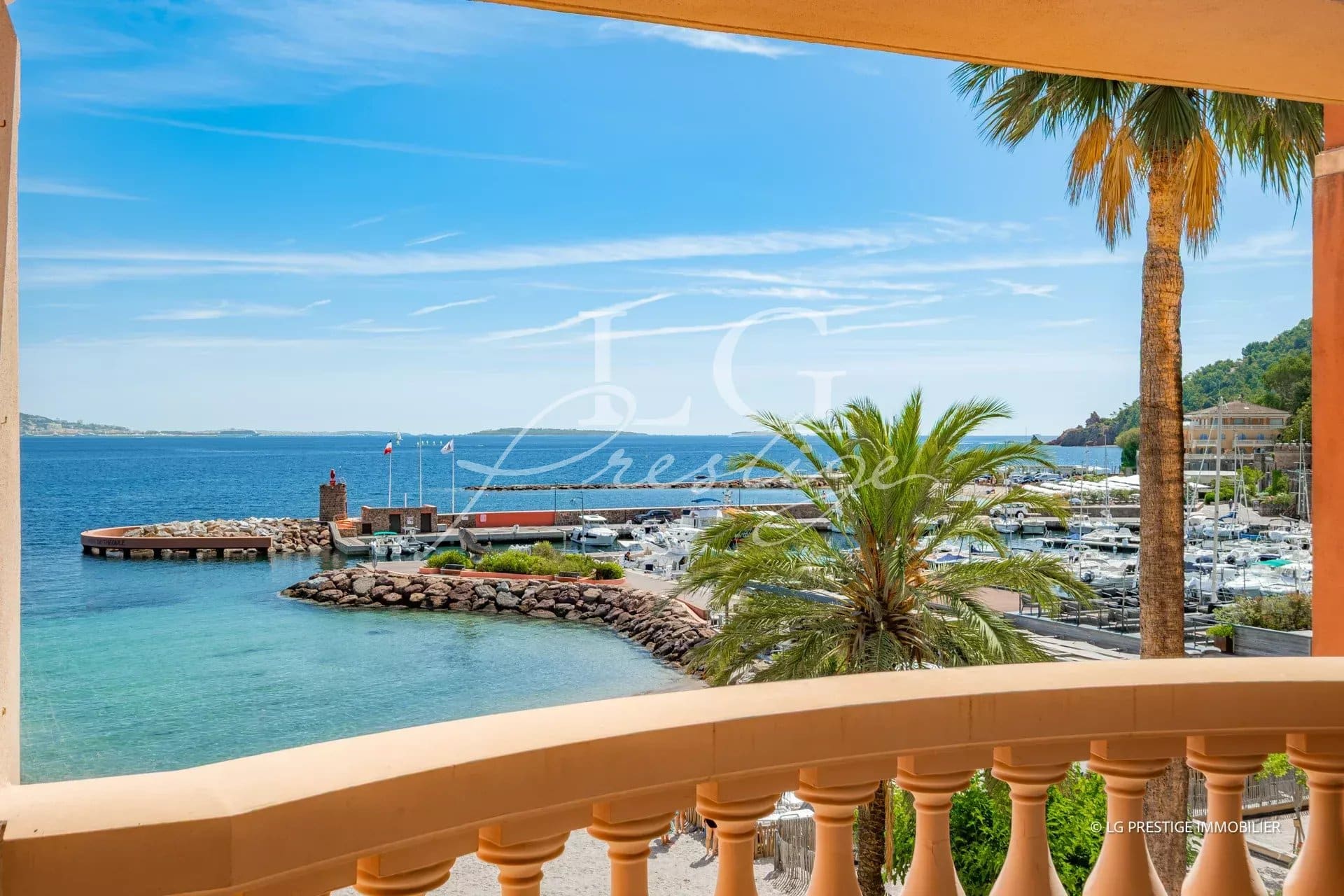 Panoramic sea view from an apartment terrace in Théoule-sur-Mer, with palm trees and port in the background.