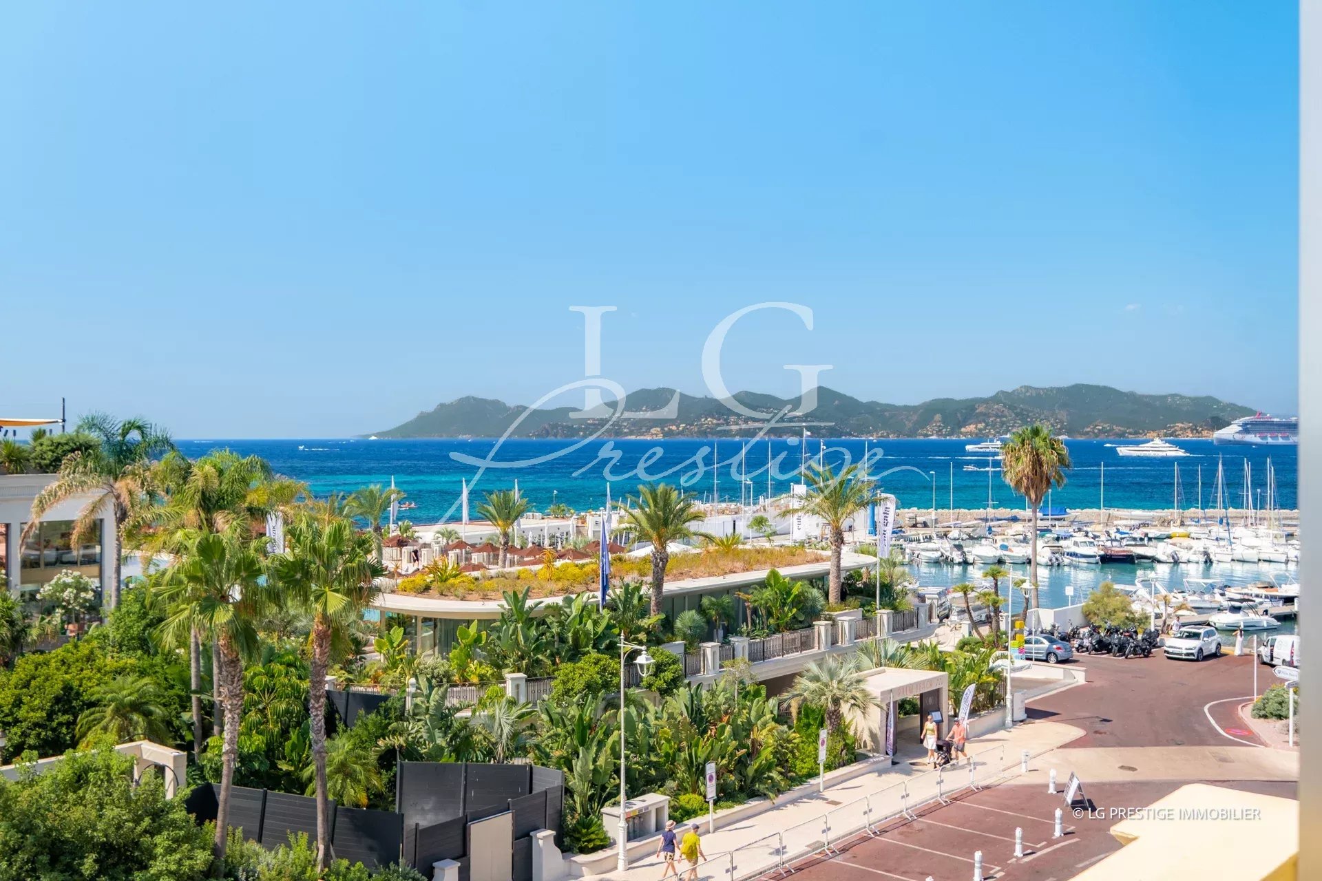 Vue de la mer depuis la Pointe Croisette à Cannes, avec des yachts au port et des palmiers.