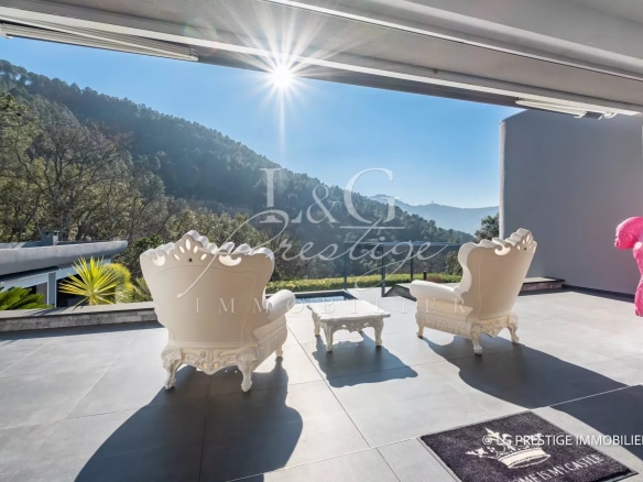 Terrasse d'une villa contemporaine avec vue sur la nature, deux chaises blanches et piscine.