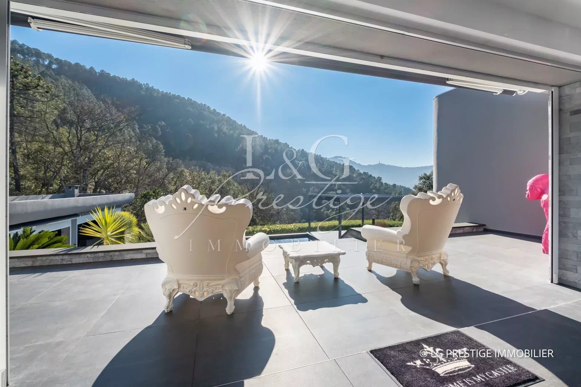 Terrasse d'une villa contemporaine avec vue sur la nature, deux chaises blanches et piscine.