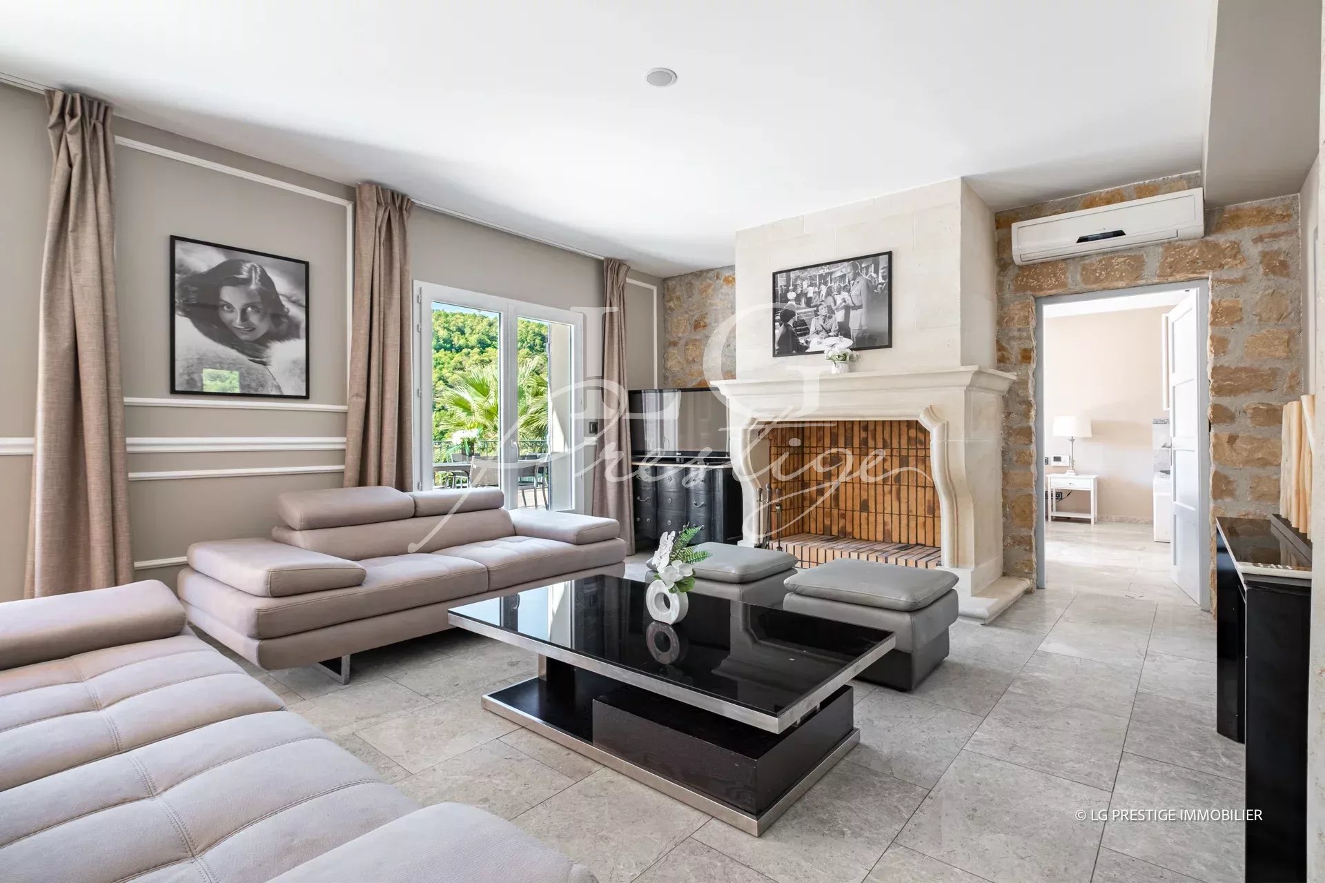Intérieur d'une maison à Grasse avec un salon moderne, cheminée et grandes fenêtres.