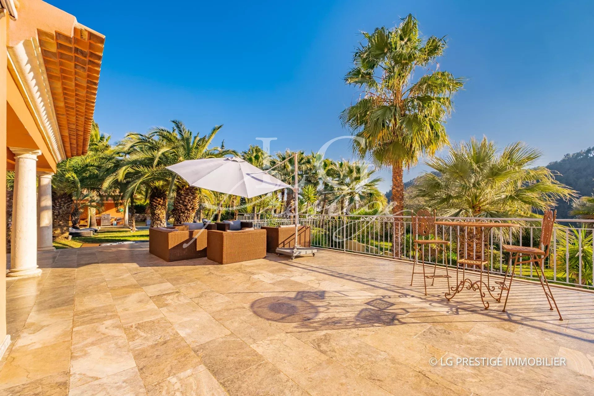 Terrasse ensoleillée avec mobilier de jardin et palmiers, vue sur la verdure à Grasse.