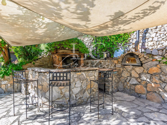 Outdoor stone bar with chairs, under an awning, in a green garden.