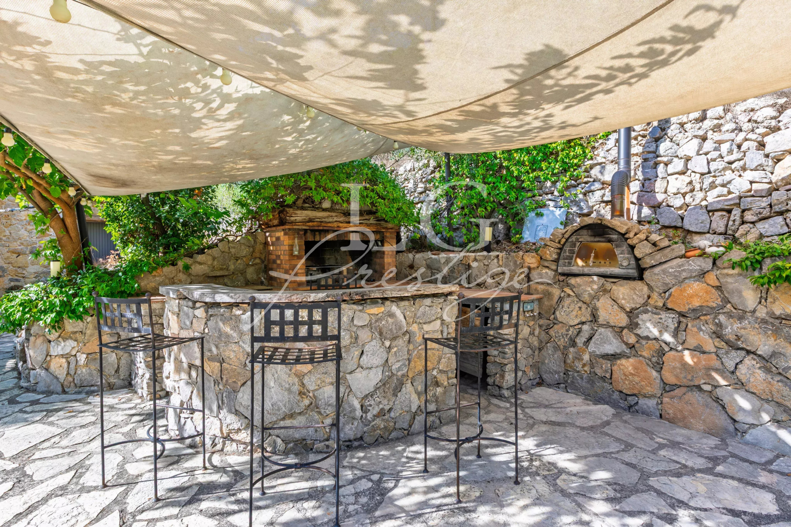 Outdoor stone bar Outdoor stone bar with chairs, under an awning, in a green garden.