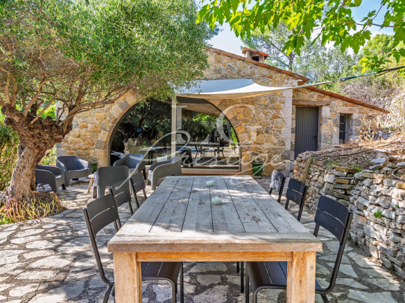 Stone terrace with wooden table and chairs, surrounded by trees and vegetation, near a Provençal villa.