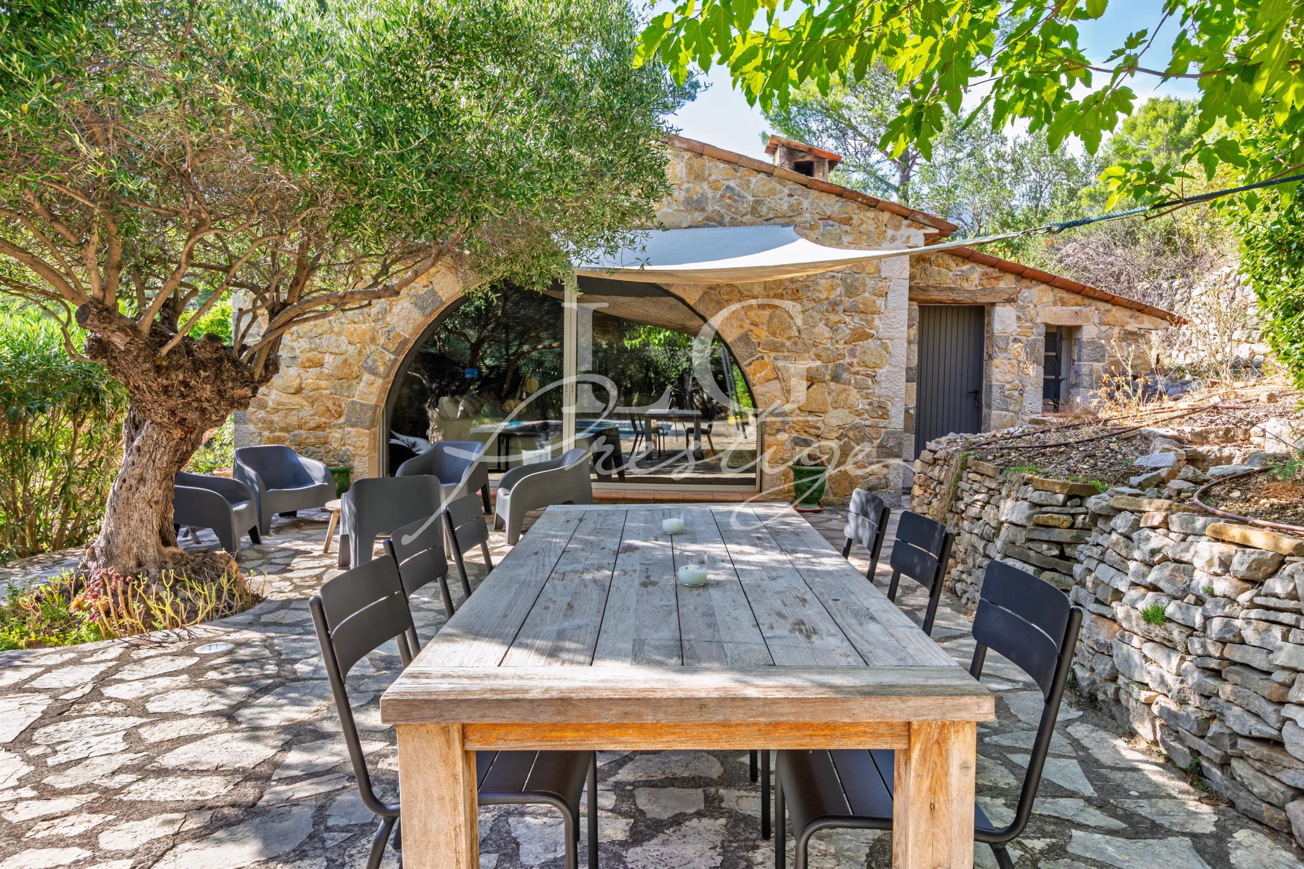 Terrace of the Provençal villa in Seillans Stone terrace with wooden table and chairs, surrounded by trees and vegetation, near a Provençal villa.