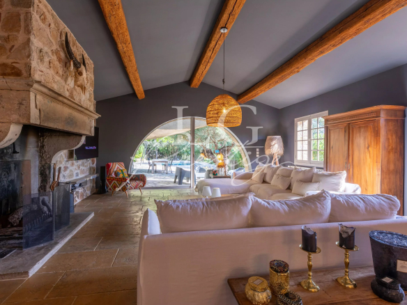 Interior of a Provençal villa with fireplace, white sofas and large windows overlooking the outside.