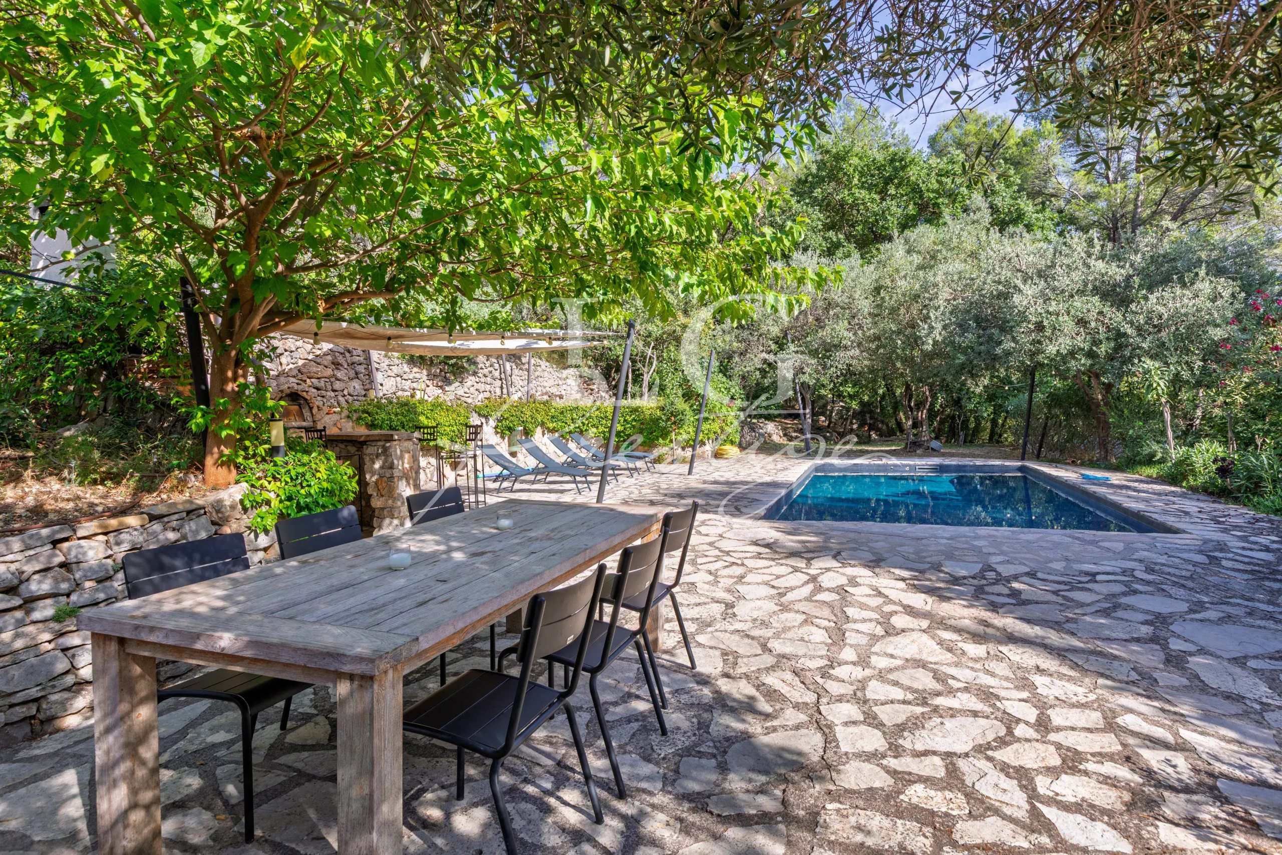 Provençal villa with swimming pool in Seillans Stone terrace with wooden table, chairs, swimming pool and lush vegetation around.