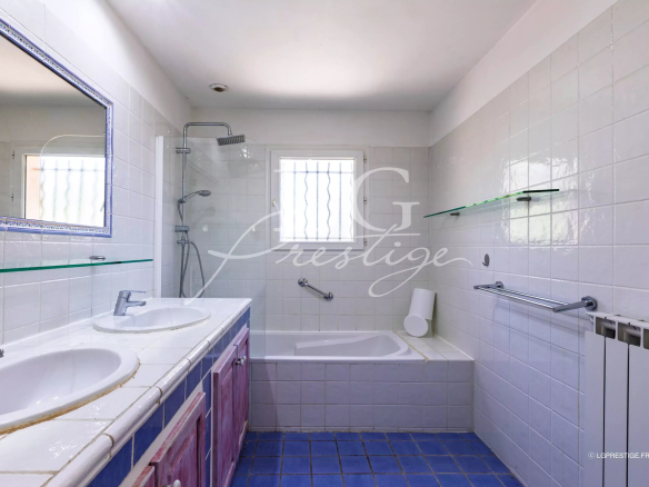 Salle de bain avec baignoire et douche, carrelage blanc et bleu, éclairage naturel.