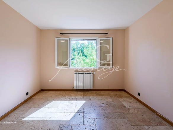 Intérieur d'une pièce vide avec fenêtres donnant sur un jardin, murs clairs et sol en pierre.