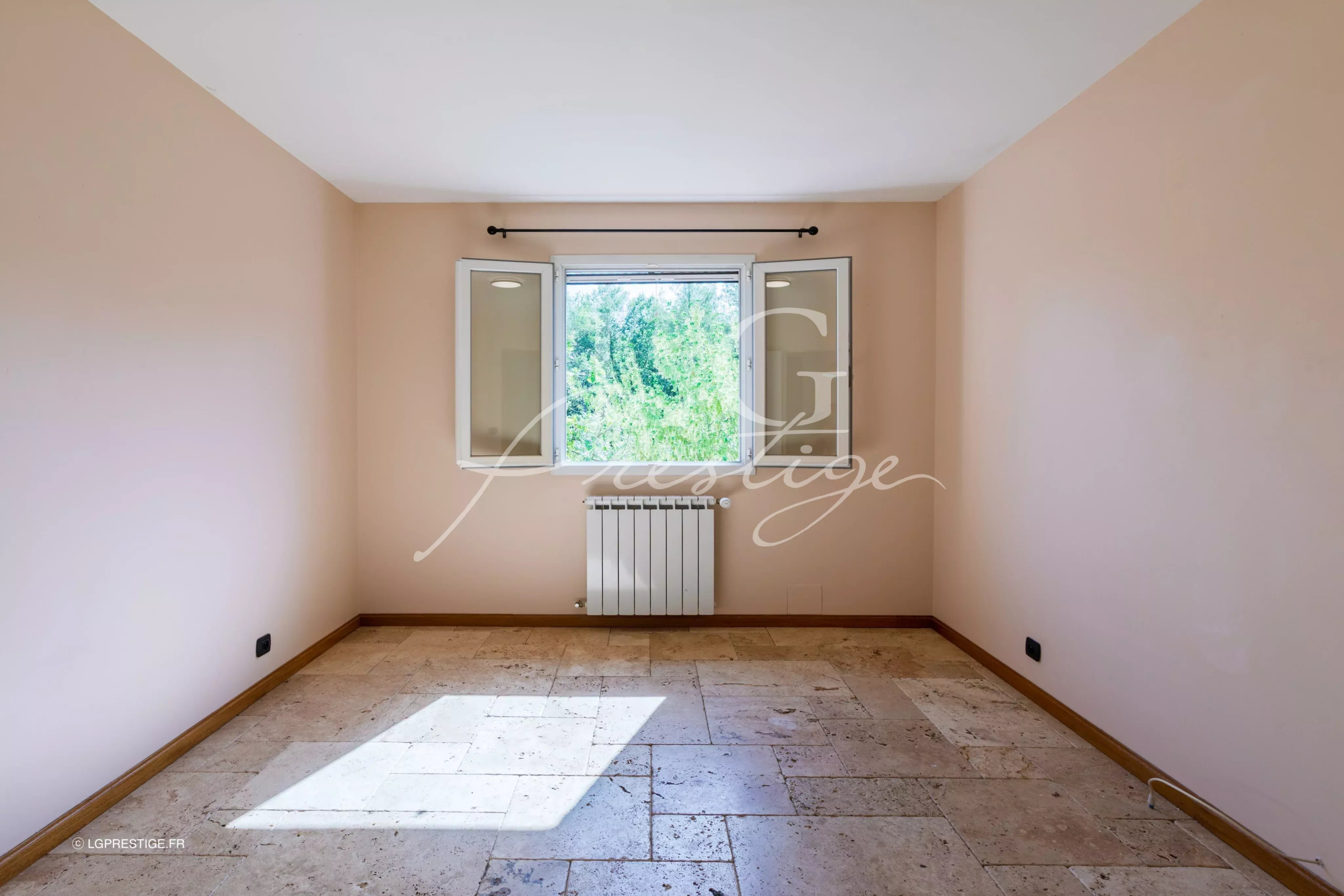 Intérieur d’une bastide provençale Intérieur d'une pièce vide avec fenêtres donnant sur un jardin, murs clairs et sol en pierre.