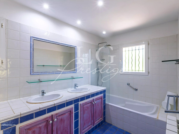 Salle de bain avec baignoire et double vasque, carrelage blanc et bleu, lumière naturelle