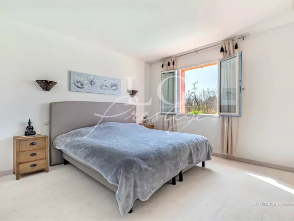 Chambre lumineuse avec un lit double et fenêtres ouvertes, décorée sobrement.