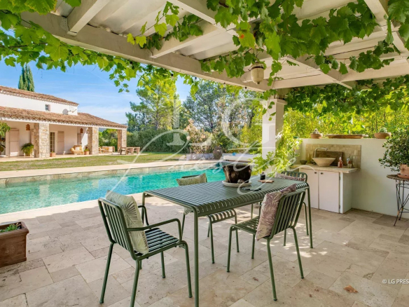 Terrasse d'une propriété provençale avec piscine, table et chaises sous un auvent de vigne à Fayence.