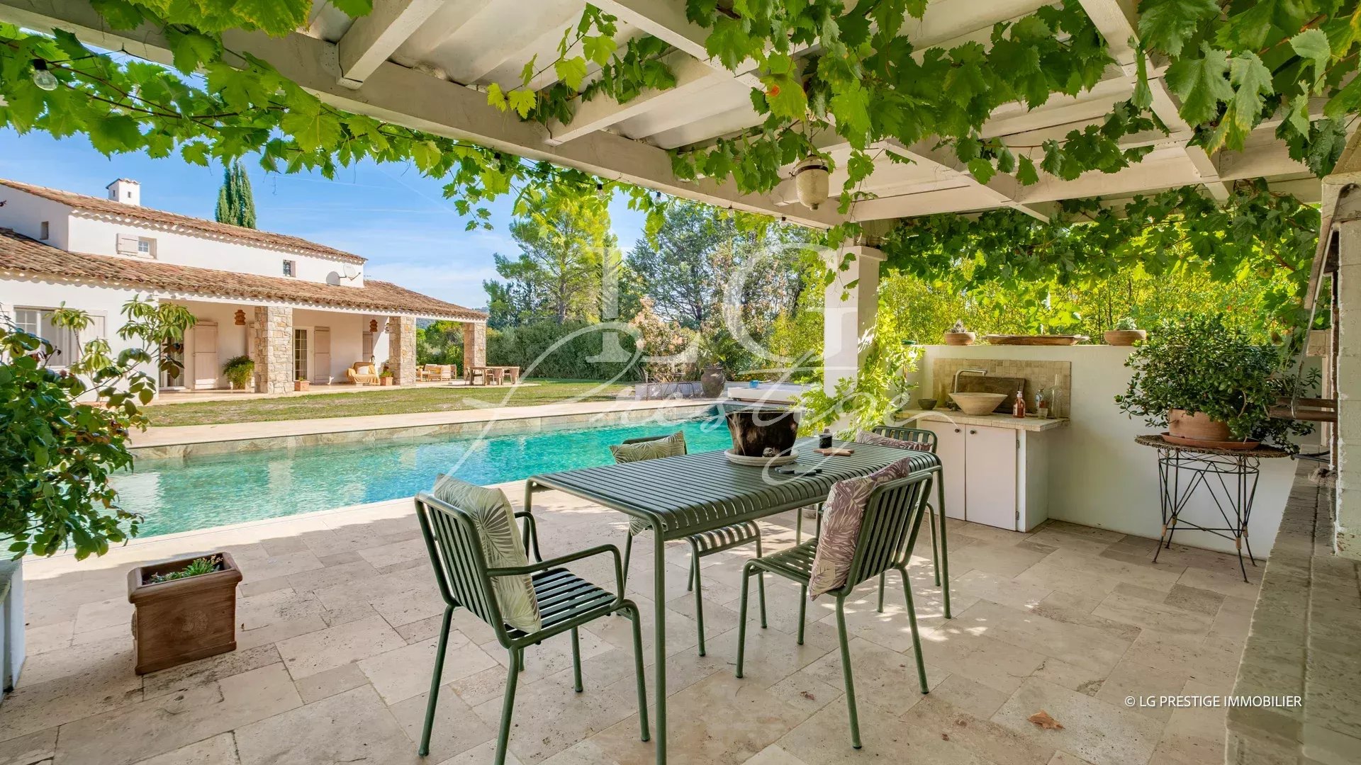 Terrasse d'une propriété provençale avec piscine, table et chaises sous un auvent de vigne à Fayence.