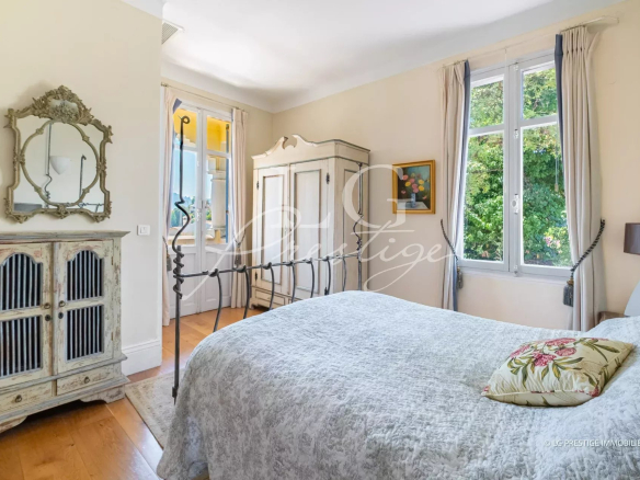 Chambre d'une villa de caractère à Mandelieu-la-Napoule, lumineuse avec des fenêtres et un mobilier ancien.