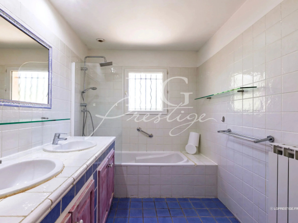 Salle de bain avec baignoire, lavabo double et douche, carrelage blanc et bleu.