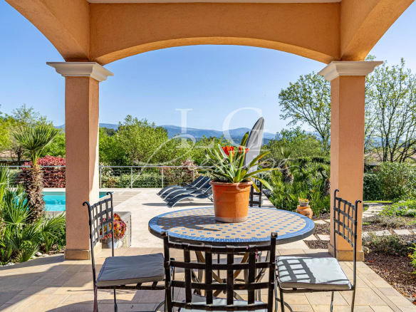 Terrasse d'une villa avec table et chaises, vue sur piscine et paysage verdoyant à Fayence.