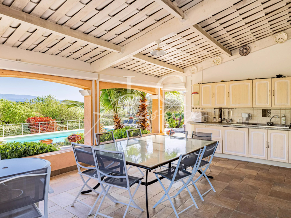 Terrasse couverte avec table et chaises, vue sur la piscine et le jardin de la villa à Fayence.
