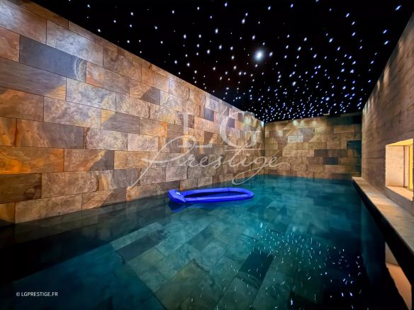Interior of a villa with swimming pool and stone wall, starry sky lighting on the ceiling.