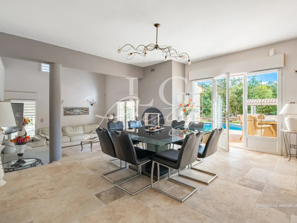 Salle à manger moderne avec table en verre et chaises noires, ouverte sur l'extérieur.