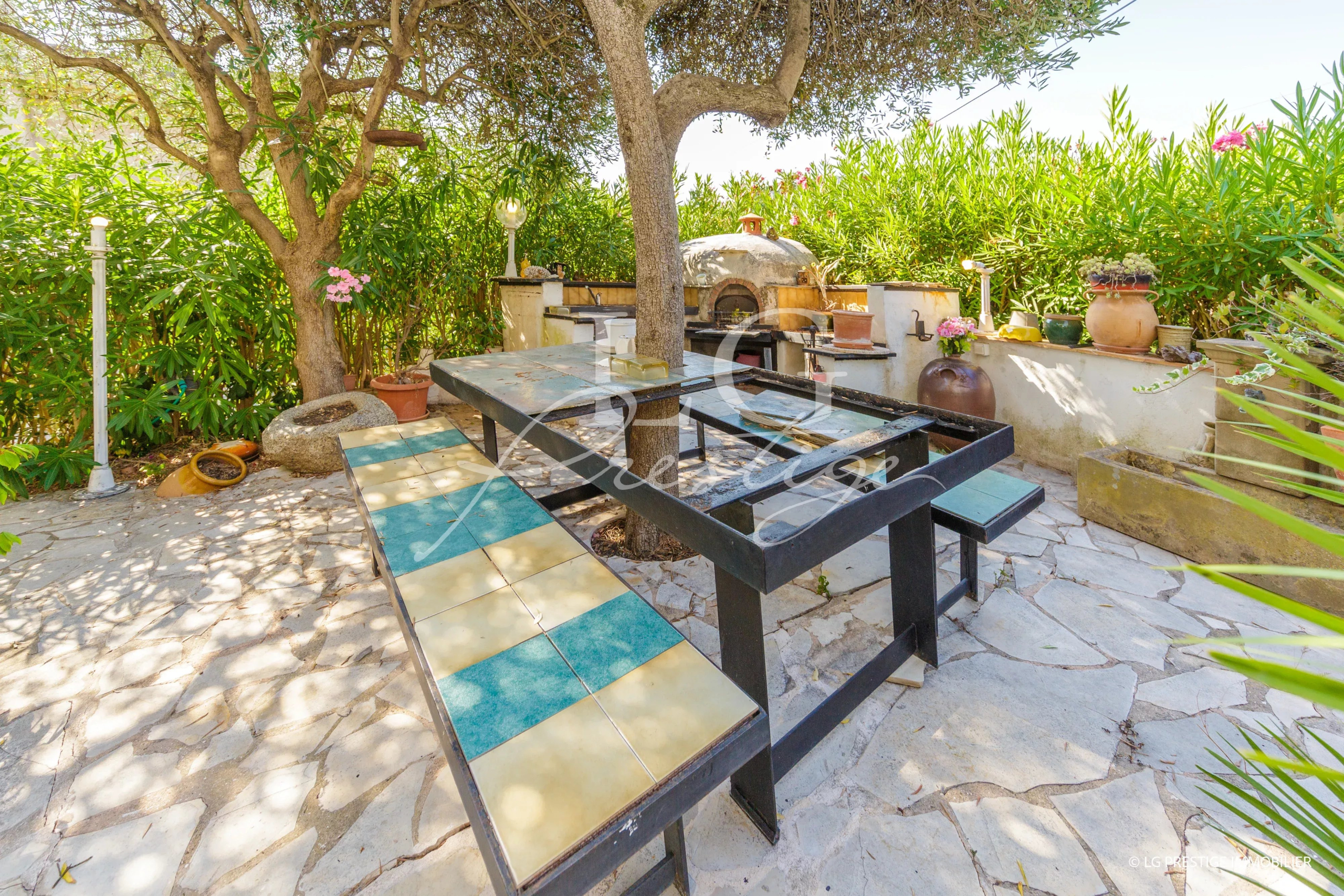 Espace extérieur d'une villa avec table en pierre et arbres, situé à Mandelieu-la-Napoule.