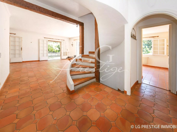 Interior of a villa to be renovated with a wooden staircase and a terracotta floor.