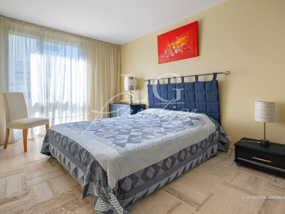 Chambre d'un appartement à Mandelieu-la-Napoule avec lit double et fenêtre laissant entrer la lumière.