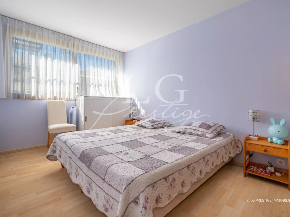 Chambre d'un appartement avec lit double et fenêtres laissant entrer la lumière.