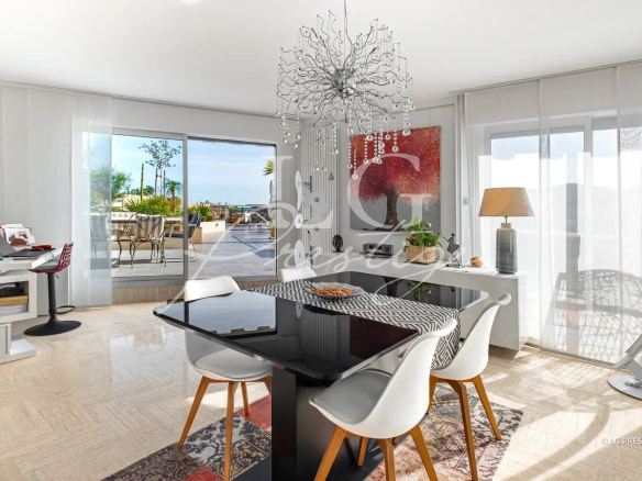 Intérieur d'un appartement lumineux avec salle à manger et accès à une terrasse. Vue sur la mer.