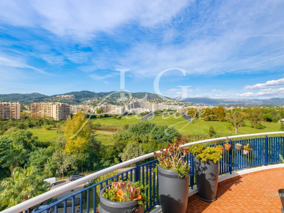 Vue panoramique depuis une terrasse d'appartement à Mandelieu-la-Napoule, avec verdure et montagnes en arrière-plan.