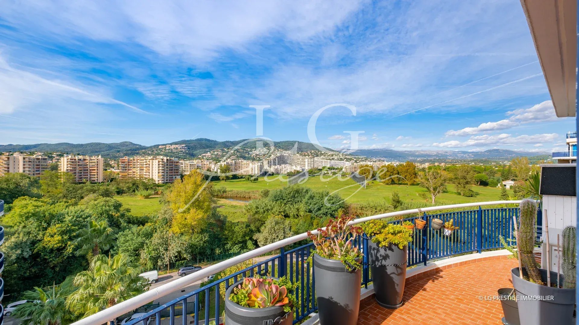 Vue panoramique depuis une terrasse d'appartement à Mandelieu-la-Napoule, avec verdure et montagnes en arrière-plan.