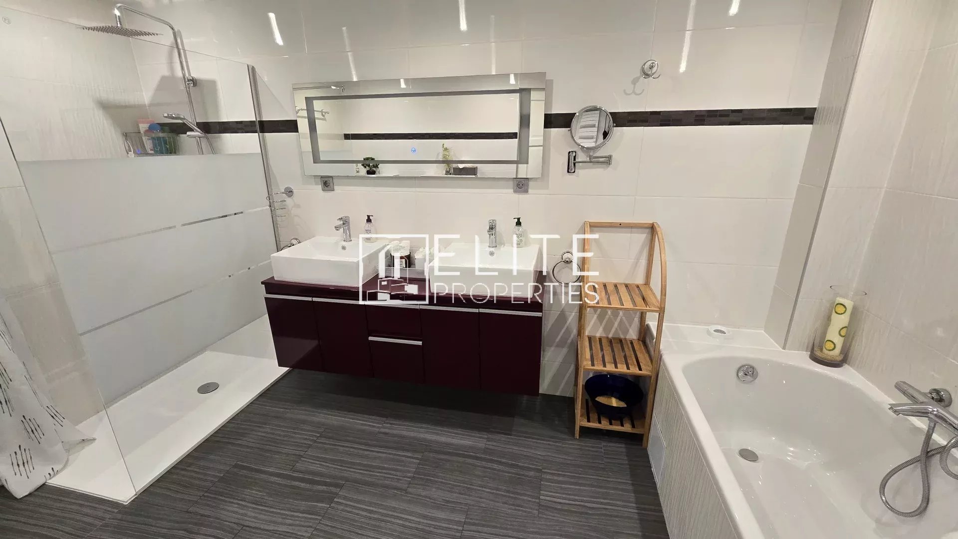 Modern bathroom with double sink vanity, glass shower, and white bathtub; wooden shelf beside tub.