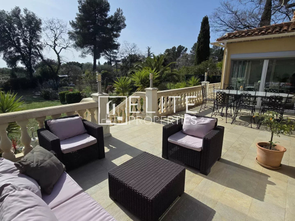 Outdoor terrace with wicker seating area and beige cushions overlooking a lush garden. A glass door leads to the interior.
