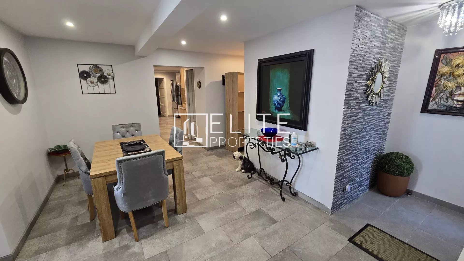 Dining area with a wooden table and four gray upholstered chairs, accented by wall art and a stone feature wall in a modern home.