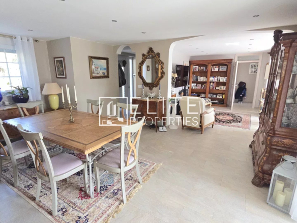 Spacious dining area with a wooden table and six chairs, beige walls, and decorative antiques along a sideboard and mirror.