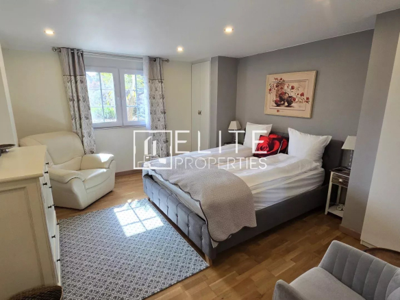 Bedroom with a gray upholstered bed, white bedding, red cushions, bedside tables, and a window with patterned curtains.