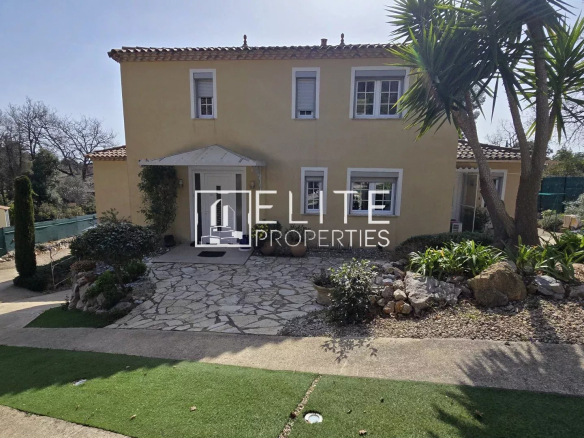 Two-story beige house with tiled roof and white-framed windows, front entrance under a small awning, stone path leading to the door, and landscaped yard.