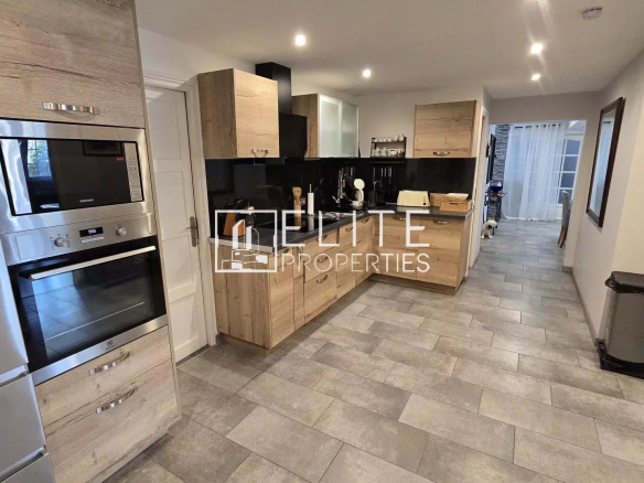 Modern kitchen with stainless steel fridge and double oven, light wood cabinets, and gray tiled floor.