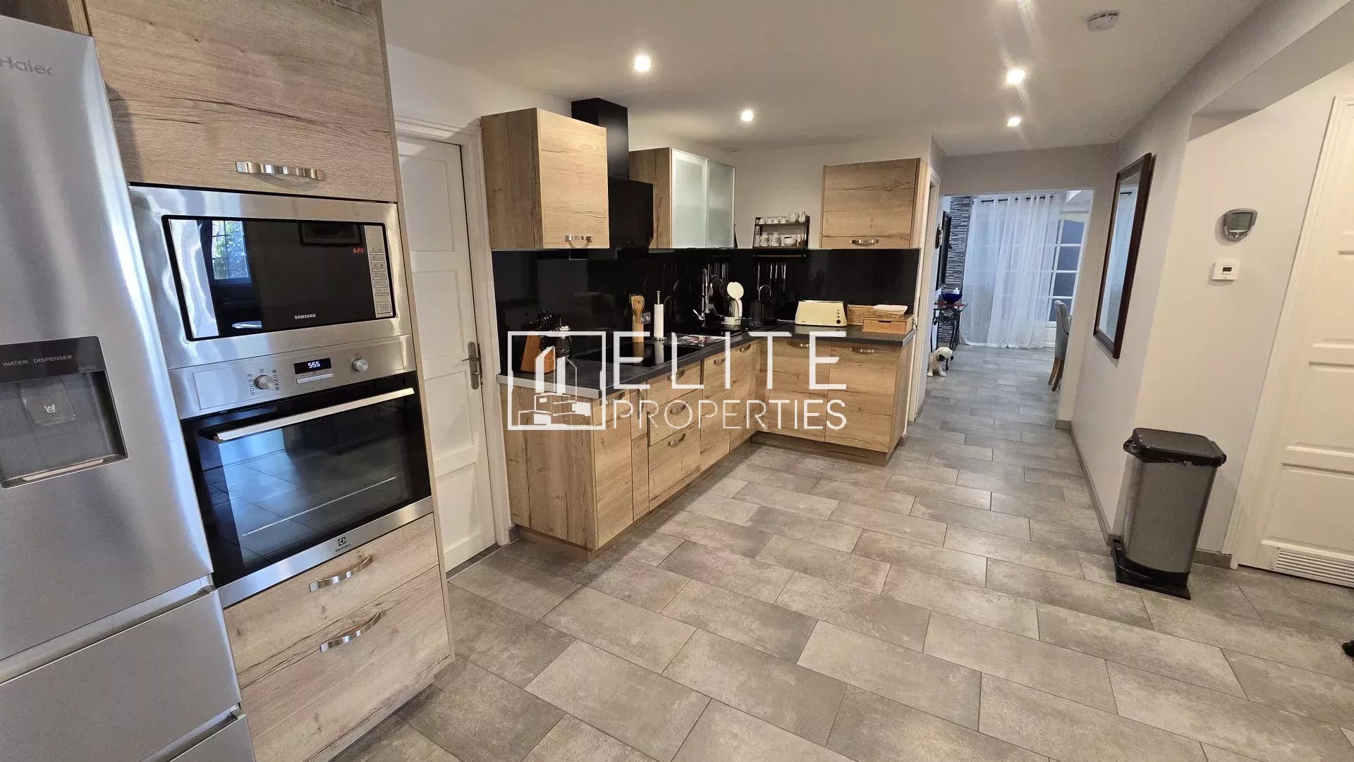 Modern kitchen with stainless steel fridge and double oven, light wood cabinets, and gray tiled floor.