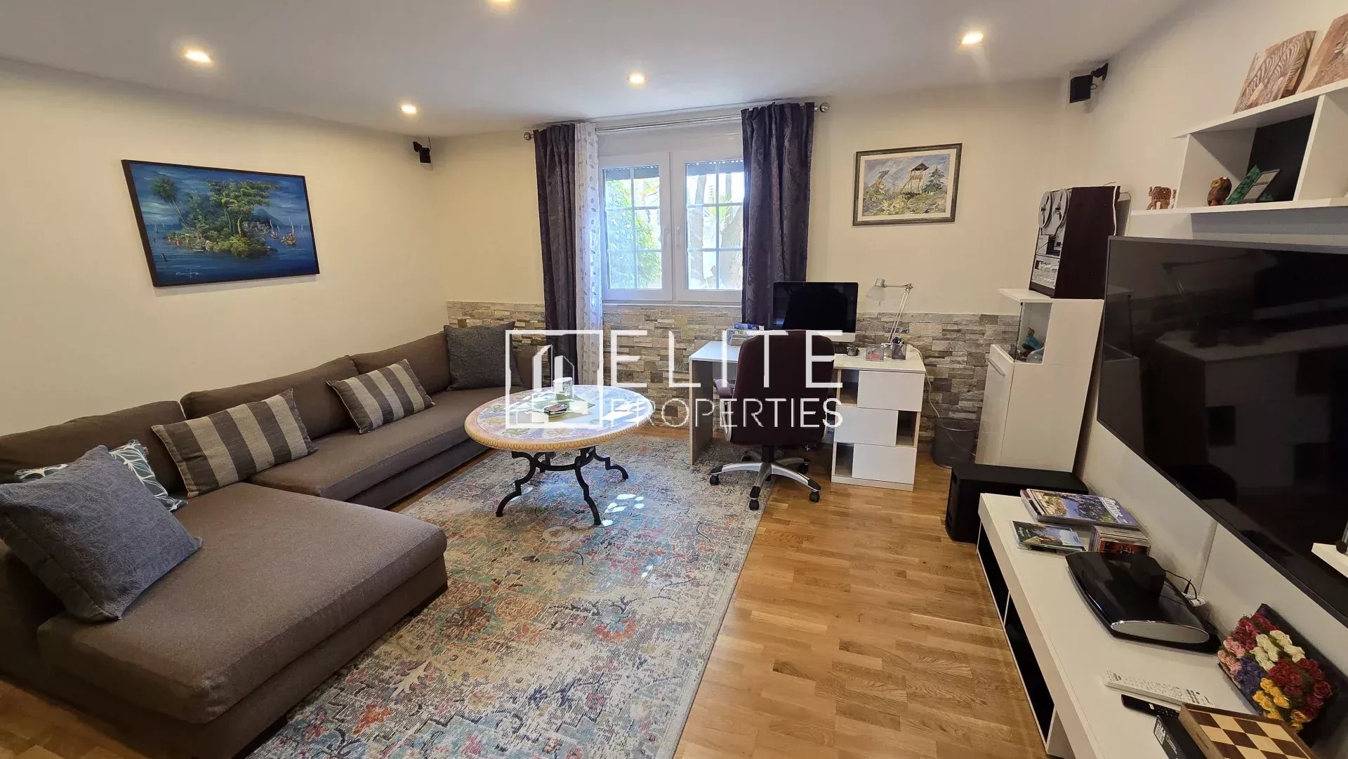 Cozy living room with an L-shaped brown sofa, striped cushions, a round coffee table, and a colorful patterned rug across hardwood floors.