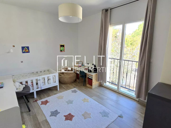 Bright child’s bedroom with a white bed, desk, and star-pattern rug beside a large window with beige curtains.