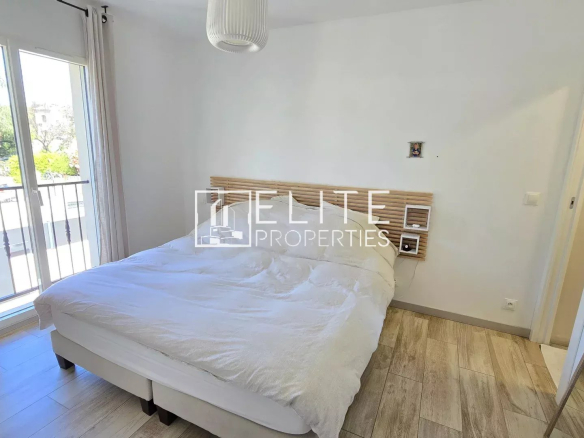 Bright bedroom with a double bed, white bedding, and a wooden slatted headboard near a balcony door.