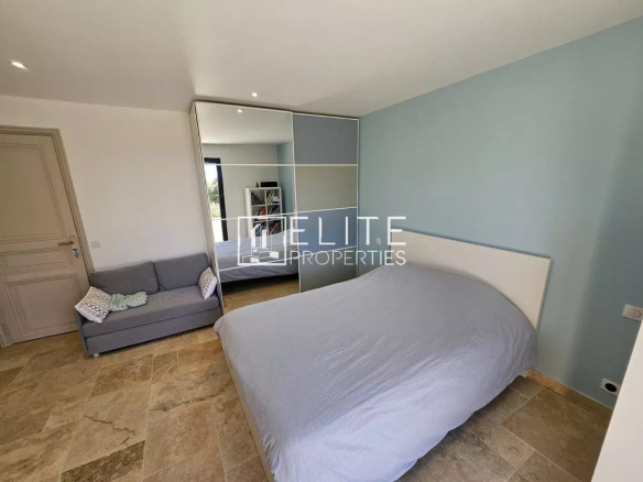 Room in a spacious house with a double bed and sofa, light walls and stone floor.