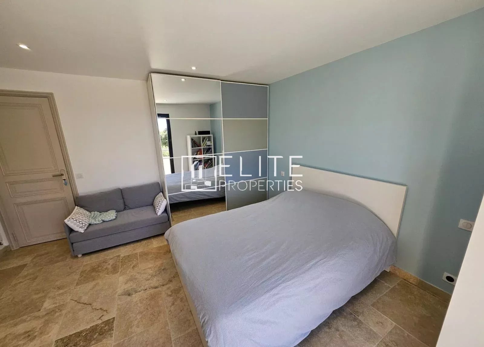 Room in a spacious house with a double bed and sofa, light walls and stone floor.