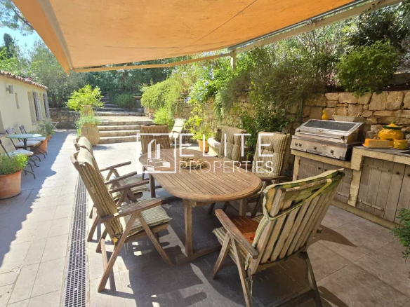 Outdoor terrace with wooden table and chairs, surrounded by greenery.