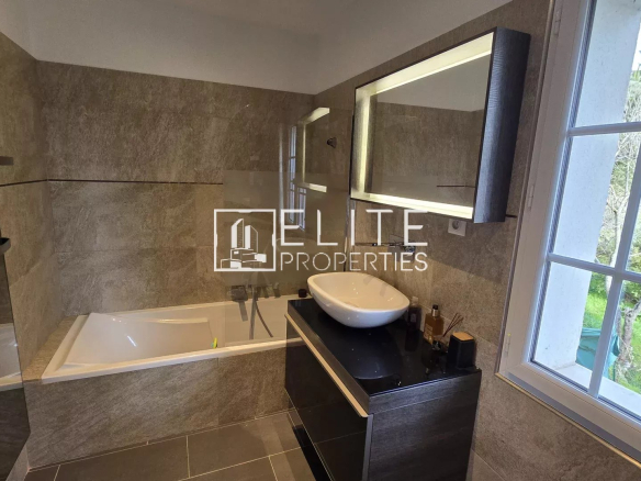 Salle de bain moderne avec baignoire et lavabo, fenêtres donnant sur l'extérieur.