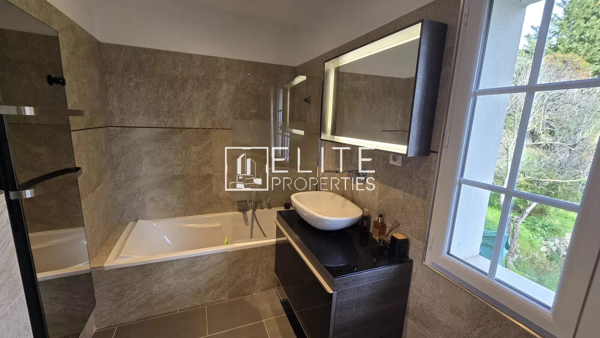Salle de bain moderne à Cabris Salle de bain moderne avec baignoire et lavabo, fenêtres donnant sur l'extérieur.