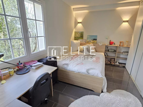Chambre lumineuse avec bureau et lit, fenêtres offrant une vue sur la nature.