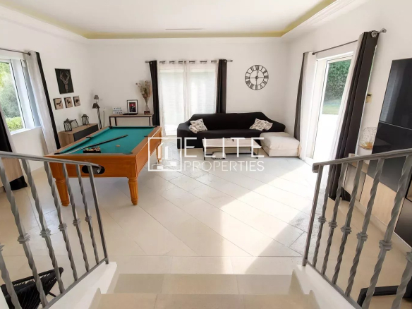 Interior of a villa with a pool table, a sofa and windows overlooking the outside.